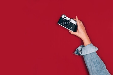 Female hand holding old retro photo camera on red background with copy space for text. Trendy...