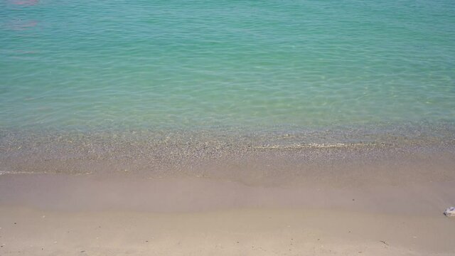 Clear turquoise ocean or sea water flowing on yellow sandy shore with small stones