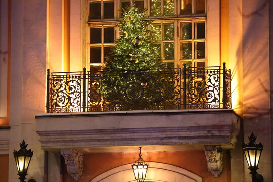 The festive Christmas tree on the balcony is decorated with golden balls and glowing lights reflected in the window at night.The tree is lit up in the dark.Beautiful image of Christmas and New Year