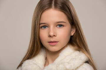 portrait of a beautiful child girl with long beautiful hair styled in a hairstyle and a fur white...
