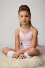 Fototapeta na wymiar beautiful child girl in a pink dress for ballet posing sitting on a white sheepskin skin in the studio on a light gray background