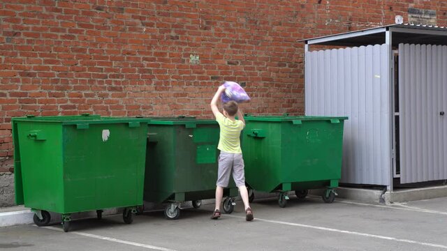 4K. A 10-year-old European boy throws food waste in blue plastic bags into a green trash can.