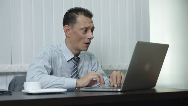 A business man who is a company employee using a laptop to work in an office intensely shocked by his job failure, disappointment and loss in his business anxiously.