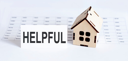 Closeup of house wooden model with blank for text HELPFUL on chart background.