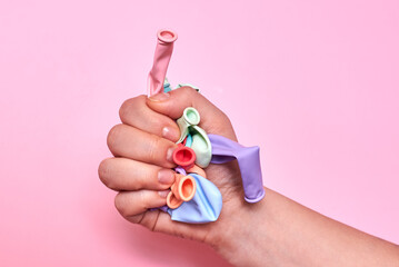 Multicolored not inflated balloons in the hands of a woman on a pink background.