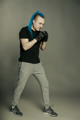 A man with an unusual hairstyle of mohawk from blue braids in boxing gloves poses and is ready for battle on a dark