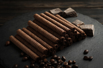 Tray with chocolate wafer rolls, coffee beans and chocolate on wooden background
