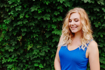 Beautiful young girl smiles in a blue dress, against a background of hedges of wild grapes. Copy space.