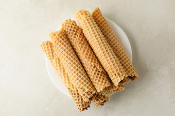 Plate with wafer rolls with condensed milk on white textured background