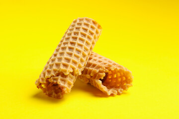 Tasty wafer rolls with condensed milk on yellow background