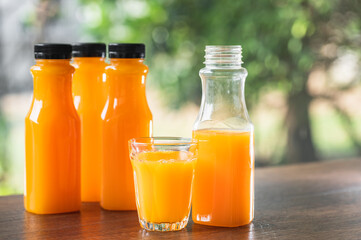 Fresh orange juice in no label clear plastic bottle with black cap on wooden table, natural trees blur in the background. With copy space.