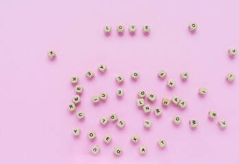 Wooden cubes with the word love on a light pink background next to other wooden cubes with letters. Valentine's day or wedding concept. Flat lay, top view. Love concept.