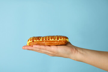 Female hand hold tasty eclair on blue background