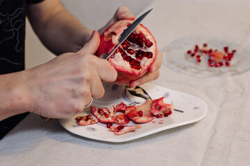 Man peels a pomegranate fruit with a knife on a plate