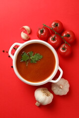 Bowl with tomato soup and ingredients on red background
