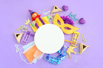 Purim celebration concept (jewish carnival holiday) over purple background. Top view, Flat lay. Coronavirus prevention concept, medical mask and sanitizer gel