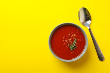 Bowl of tasty tomato soup and spoon on yellow background