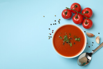 Bowl with tomato soup and ingredients on blue background