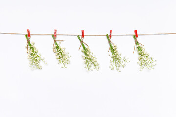 Creative spring composition with small bouquets of lilies of the valley flowers hanging on rope by clothespins on white background. Springtime concept, mock up for greeting card, copy space