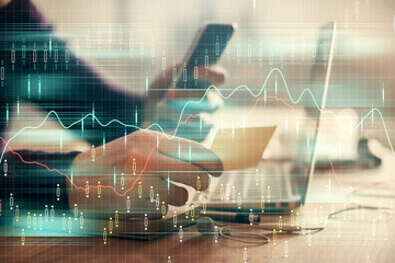 Double exposure of man's hands holding and using a phone and financial graph drawing. Analysis concept.
