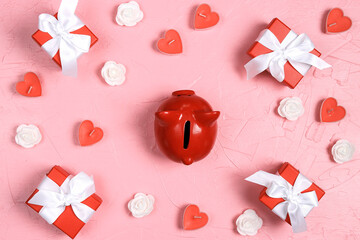 Piggy bank surrounded by gifts, candles hearts and roses on pink background.