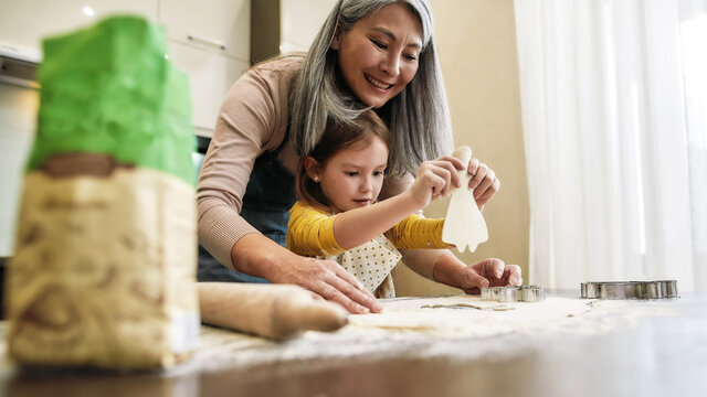 Little granddaughter holding raw cookie near grandmother - Powered by Adobe