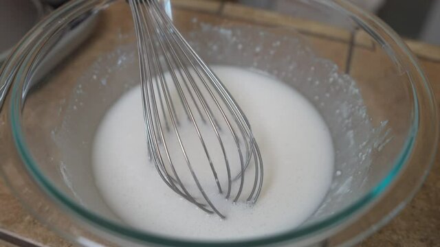 Whisk Sits In Glass Bowl Of White Icing Or Sugar Glaze, Closeup Detail