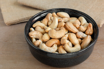 close up of homemade style roasted cashew nuts in a ceramic bowl on wooden table.