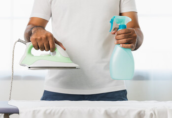 Man's hand holding a spray bottle and iron To iron the fabric to make it smooth. Pictures about...