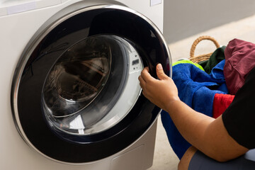 Man's hand opening the front of the washing machine And is about to put the dirty laundry into the wash