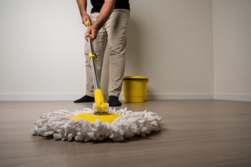 Close up young man holding the yellow wet mop to cleaning the wooden floor in the living room in...