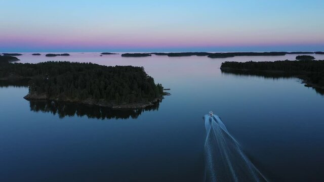 Aerial view following a motorboat driving in middle of islands, vibrant dusk sky in the Scandinavian archipelago - dolly, drone shot