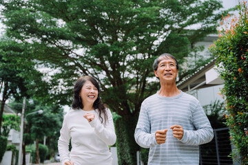 Cheerful asian senior couple jogging exercising outdoors at park.