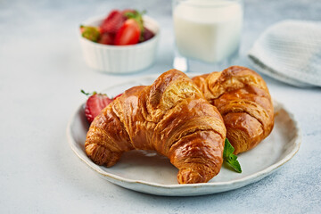 Croissant on a plate with strawberries and glass of fresh milk