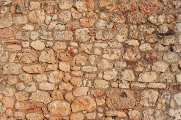 Rough reddish color stone bricks wall, sun shines on