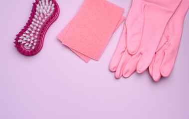 Pink rubber gloves for cleaning, pink sponges, brushes on a purple background