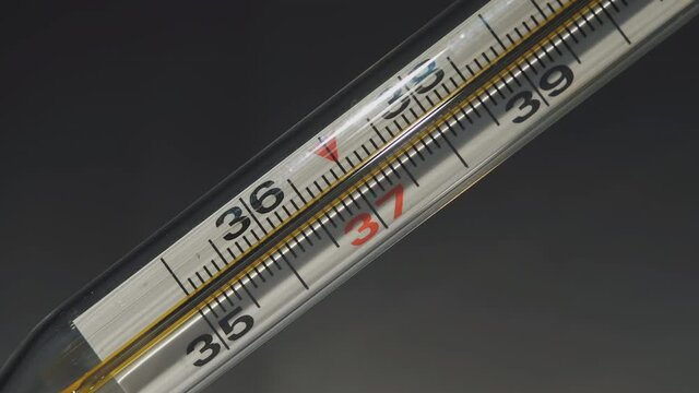 Temperature Rising Shown on a Thermometer. Glass Mercurial Thermometer Shows High Temperature of the Body. Temperature Increase and Decreases on a Thermometer. Black Background. Close Up