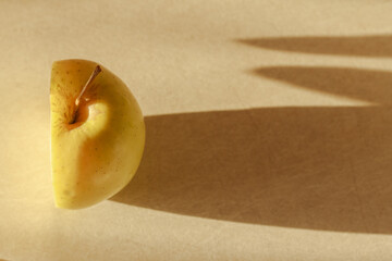 Half apple yellow and long sharp shadows on light background. Hunger concept . Copy space