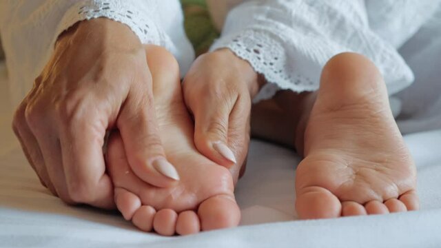 Mother massages her baby's feet close up. Mom's hands mass little children's legs. Childcare and motherhood concept.