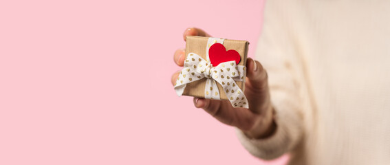 Beauty Woman hands holding Gift box with red heart on pink background, close-up. pastel colors, copy space for text. Valentine gift. Banner for Christmas, hew year, birthday concept.
