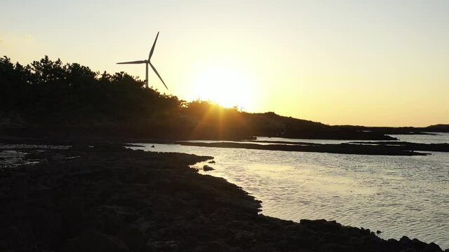 A video of a red sunset with windmills and silhouette of trees.