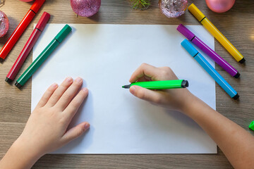 hands draws a Christmas tree with a colored felt-tip pen, sitting at the table in the classroom