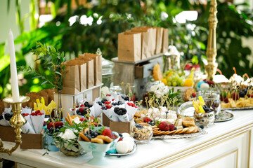 A table with delicacies-macaroons, biscuits, berries, nuts in plates, on trays and in bags.