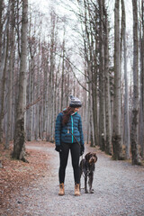 Young lady with her dog in beautiful forest on a morning walk. Connection between a dog and woman. Relationship of mutual trust. Woman with blue jacket and Rough-coated Bohemian Pointer, Czech breed