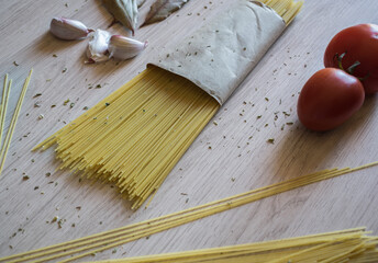 Fototapeta na wymiar Bundle of Italian spaghetti pasta tied with tomatoes, garlic, onion, oregano and bay leaves on a wooden background