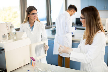 Female scientists in a white lab coat putting vial with a sample for an analysis on a ionchromatography system in biomedical lab