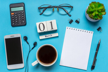 Office workplace with coffee cup, smart phone, calculator, stationery and plant. Date 01 March on wooden block calendar. White blank empty notepad page. Table desk top view, flat lay, copy space