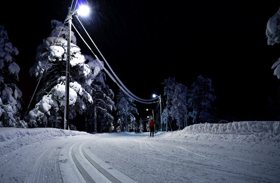 Person skiing in a cross country slope through an idyllic lit forest at night.