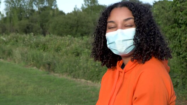 Beautiful mixed race African American girl teenager young woman wearing a face mask during COVID-19 Coronavirus pandemic using her smartphone or cell phone for social media