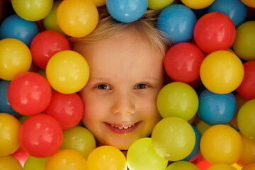 Fototapeta na wymiar Smiling girl with colourful balls - Colourful balls and girl playing with the balls - Focus on mouth. Happy children playing and having fun at kindergarten with colourful balls - Happy girl with balls